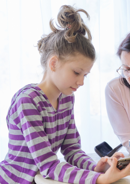 Preteen child girl at meeting with speech-language pathologist showing her smartphone to therapist.